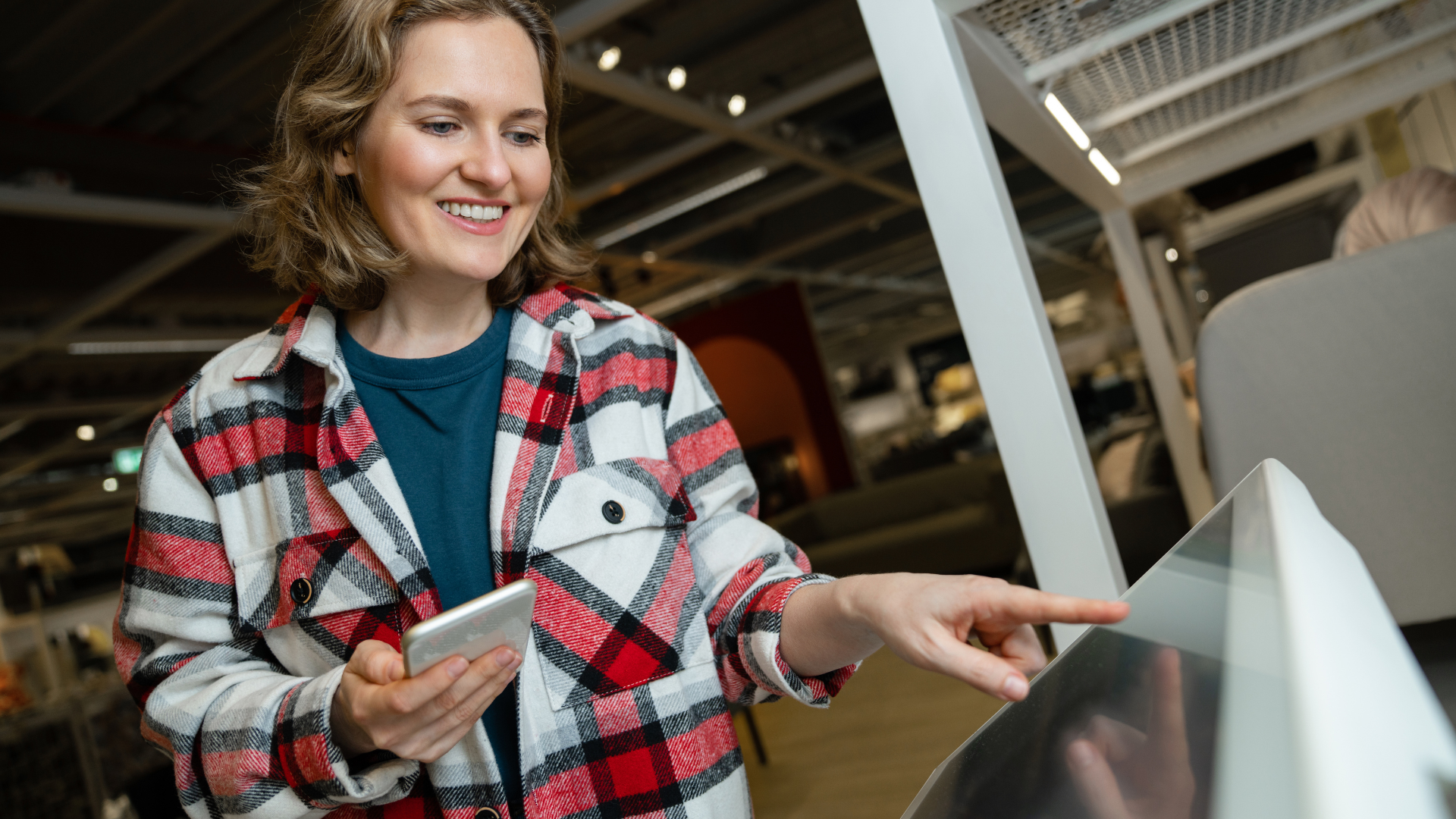 Happy customer using a self-service kiosk for a fast 30-second checkout while holding a smartphone in a modern store.